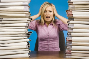 stock photo of a woman sitting between two huge stacks of files looking stressed
